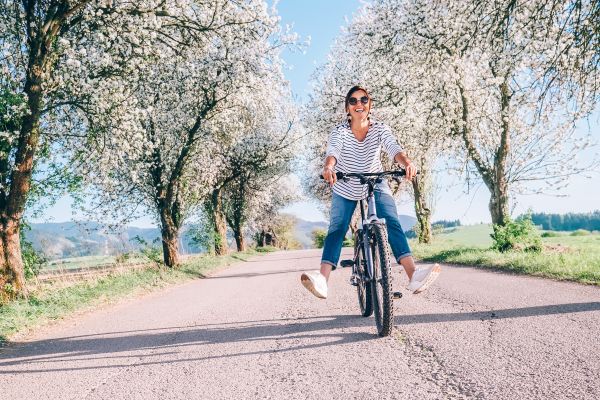 Happy smiling woman rides a bicycle on the country road under the apple blossom trees
